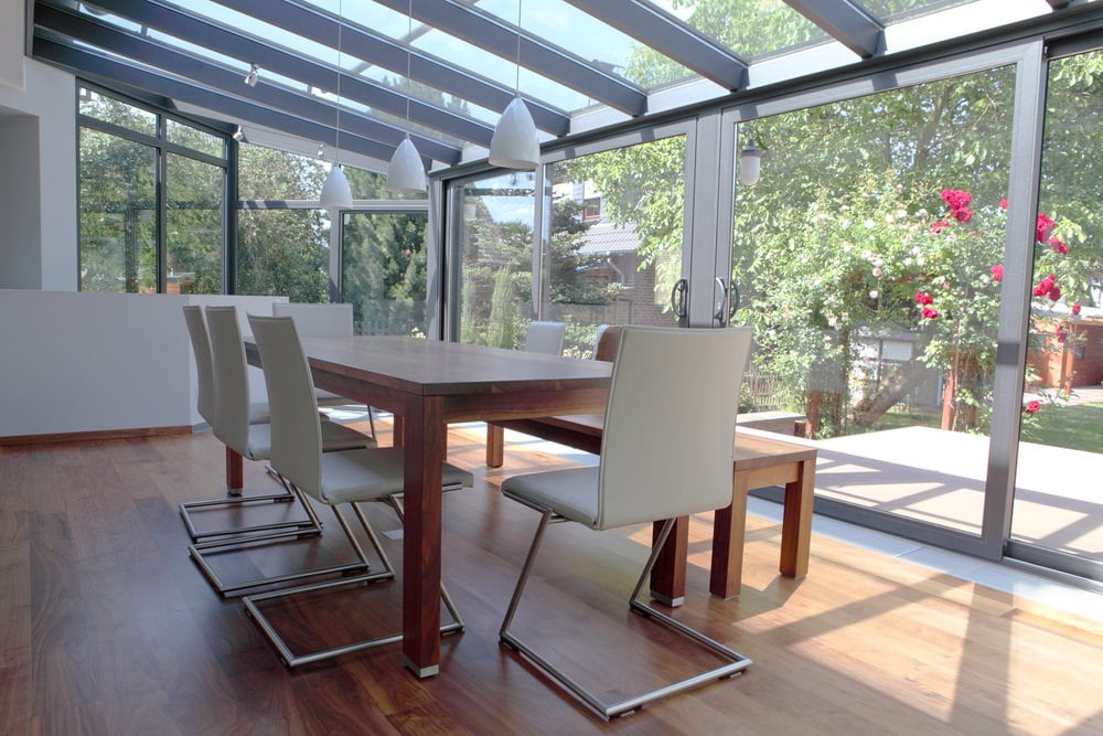 A contemporary sunroom with hardwood floor, glass windows and glass ceilings.