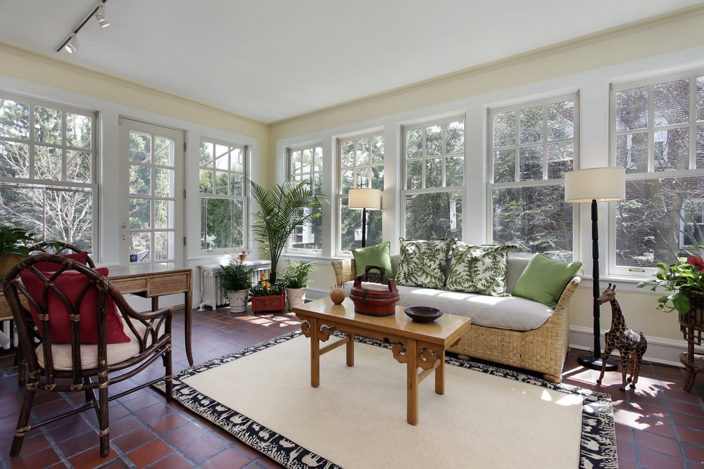 A fresh and elegant-looking living room with several glass windows, potted plants and printed throw pillows to match with the atmosphere.