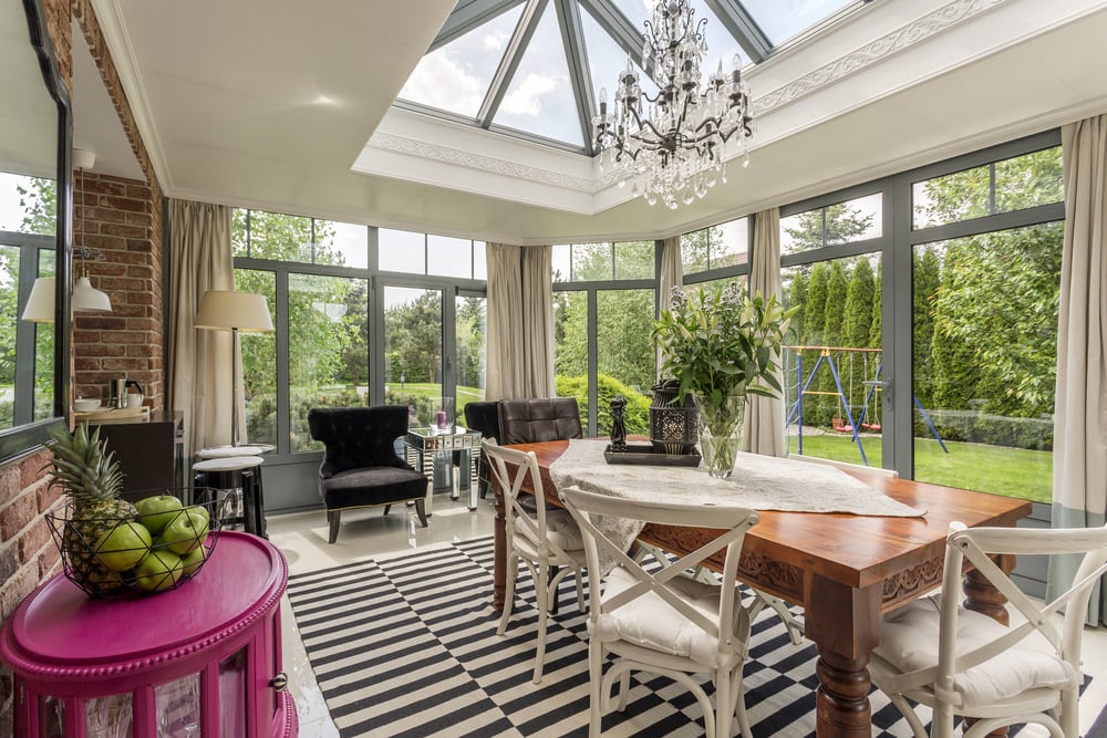 An eclectic sunroom with a garden view. The walls are made up of bricks and the floor is covered with a creative, striped carpet.
